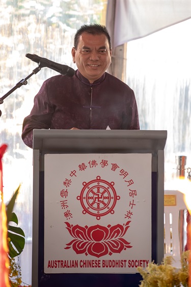 Man wearing traditional Chinese costume while standing at a podium and speaking into a microphone