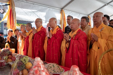 Mayor Frank Carbone standing with a group of monks while they put their hands together to pray