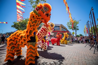 Group of lion dancers with orange, white, red and yellow costumes perform for crowd of guests
