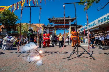 Chinese fire crackers exploding while crowd of guests cover their ears and lion dancers perform