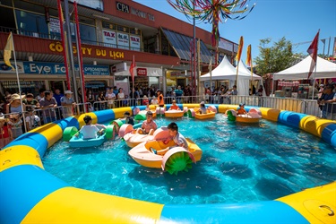 Young children in paddle boats and peddling around a large inflatable pool of water