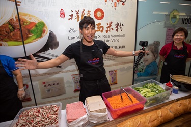 Andy Trieu smiling and posing behind a table of ingredients for making a Vietnamese bread roll