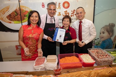 Mayor Frank Carbone, Councillor Dai Le, Councillor Adrian Wong smiling and posing while presenting elderly baker with a certificate of appreciation