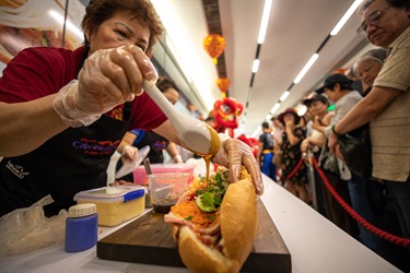 Elderly baker pouring spoons of fish sauce into Vietnamese bread roll