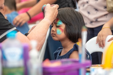Young girl getting her face painted with blue, red and yellow pattern