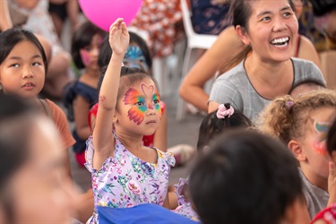 Young girl with rainbow face paint raising her arm in the crowd
