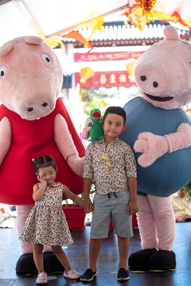 Young siblings holding hands while posing with Peppa Pig and George mascots