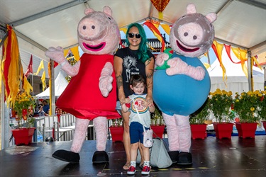 Young woman and child smiling and posing with Peppa Pig and George mascots