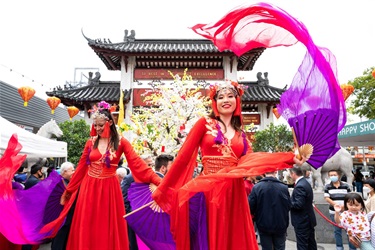 Stilt walkers in beautiful red Chinese costumes waving flowing purple fabric fans in front of Pai Lau gate.