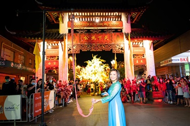 Dai Le in traditional Vietnamese Ao dai lighting fire crackers in front of a large crowd at Pai Lau gate.