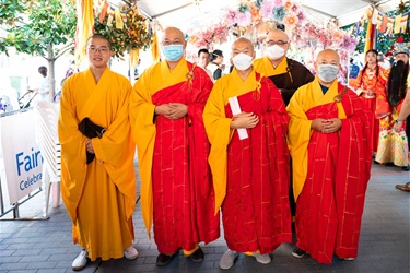 Five Buddhist monks posing and smiling for a photo. The first monk is wearing a yellow monk attire, the next three are wearing red and yellow monk attire and the last is wearing yellow and brown monk attire.