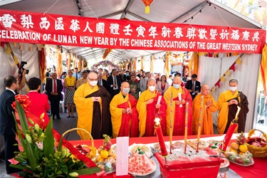 Monks in traditional monk attire praying in front of red decorated ceremonial table.