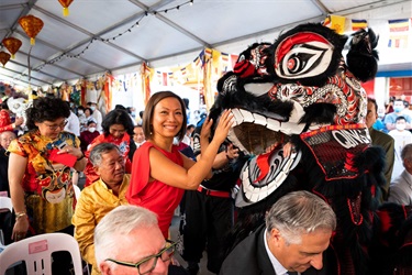 Dai Le smiling and posing for a photo with her hands on the mouth of a black and red lion dancer costume.