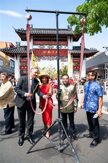 Mayor Frank Carbone and Dai Le, preparing to light fire crackers in from of the Pai Lau gate, accompanied by 3 men wearing a brown, a golden and blue traditional Chinese shirts.
