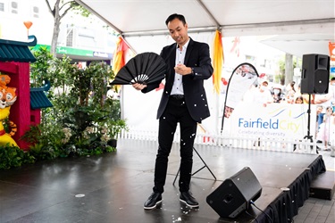 David Ung the Magician performing on Stage whilst holding a black fan