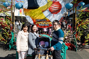 Family smiling and posing with Cabramatta Moon Festival banner and floral backdrop