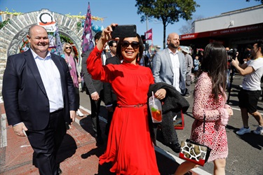 Counciller Dai Le smiling and filming on her phone while walking past the arc