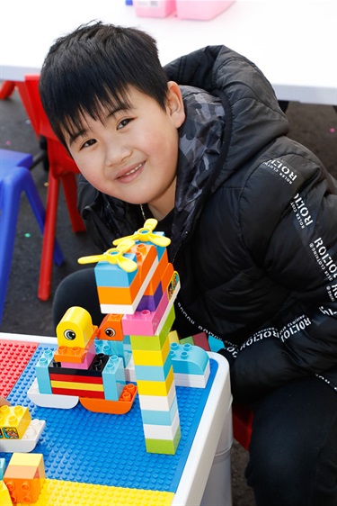 Young boy smiling and posing with colourful building brick blocks creation