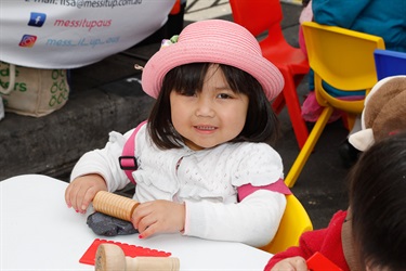 Young girl smiling and posing while using small rolling pin and flattening out black clay