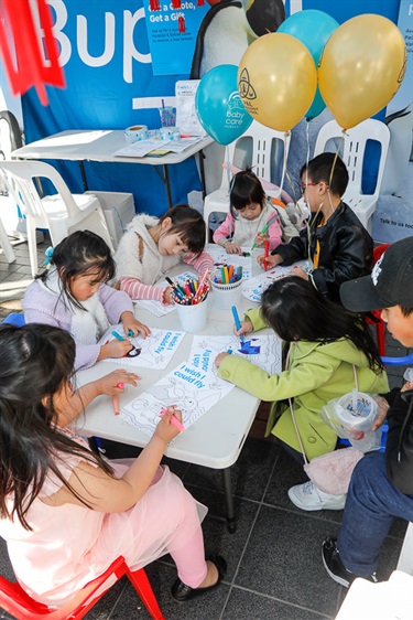 Group of young children sitting around table while using markers to colour in pictures