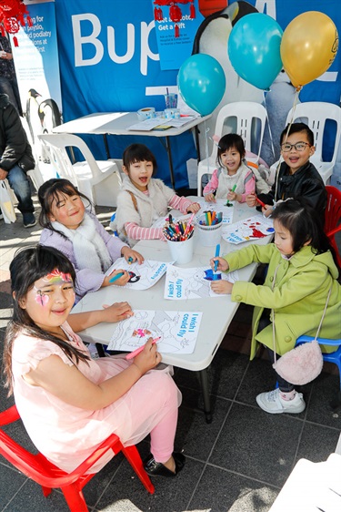 Young children smiling and posing while using markers to colour in pictures