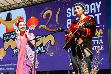 Two young women wearing different traditional cultural costume while smiling and performing on stage