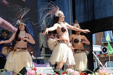 Three young women wearing traditional Polynesian costumes performing dance on the stage