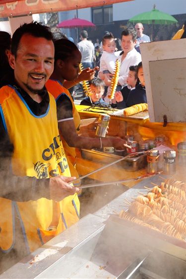 Young man smiling and posing while cooking popular festival food chips on a stick