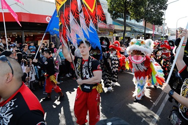 Young man holding a red and black flag leading parade of colourful lion dancing puppets