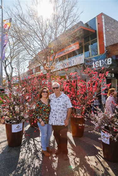 Man and woman smiling and posing in front of pink blossom trees