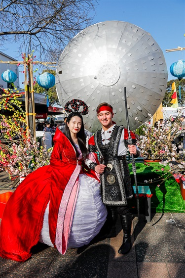 Young woman and man dressed as the Chinese Moon Goddess and Archer smiling and posing in front of Cabramatta Moon Festival decorations