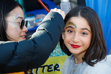 Face painter places glitter on the face of a young girl smiling and posing