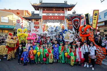 Moon Goddess and Sun Archer characters smiling and posing with a group of police officers, lion dancers and young children wearing cultural dresses