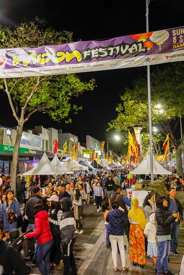 Crowd of guests walking through John Street, under red and yellow flags, at night time