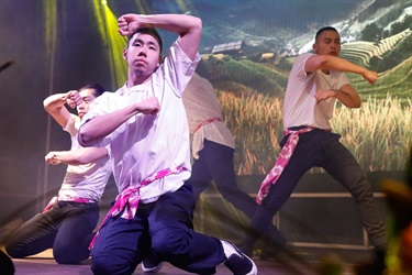 Group of young men wearing white shirts, black pants and pink floral belts performing dance on the stage