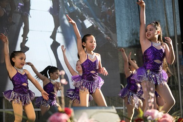 Group of young girls wearing purple costumes performing dance routine on the stage