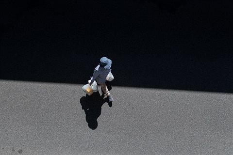 Person with blue hat walking across the street with a shopping bag in their right hand