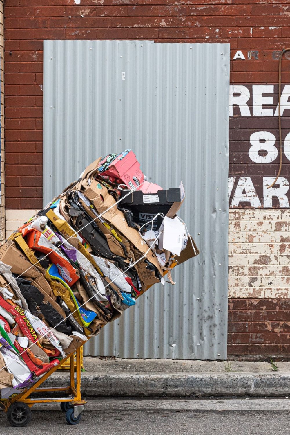 Trolley with cardboard, bound by rope in front of an industrial building.