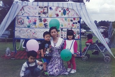 Family smiling and posing with balloons in front of colourfully painted banner at a picnic