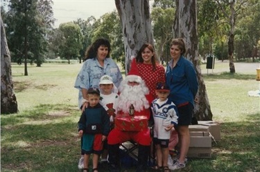 Women and young children smiling and posing with Santa