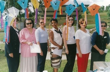 Group of women smiling and posing under colourful paper kites at launch of Childcare Benefits at Western Sydney Parklands