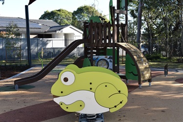 Frog shaped spring rider in front of play fortress and slide