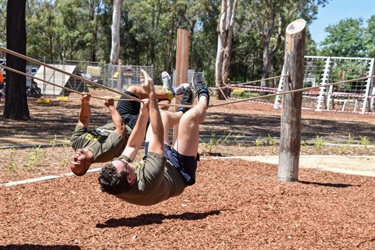 Two men climbing upside down along horizontal ropes in obstacle course
