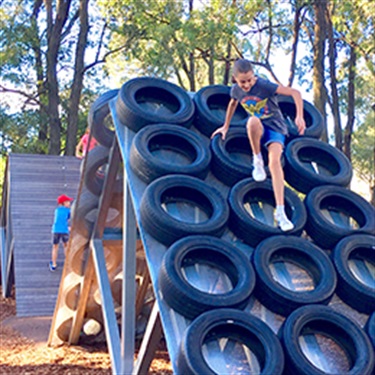 Teenager climbing over tyre obstacle in obstacle course