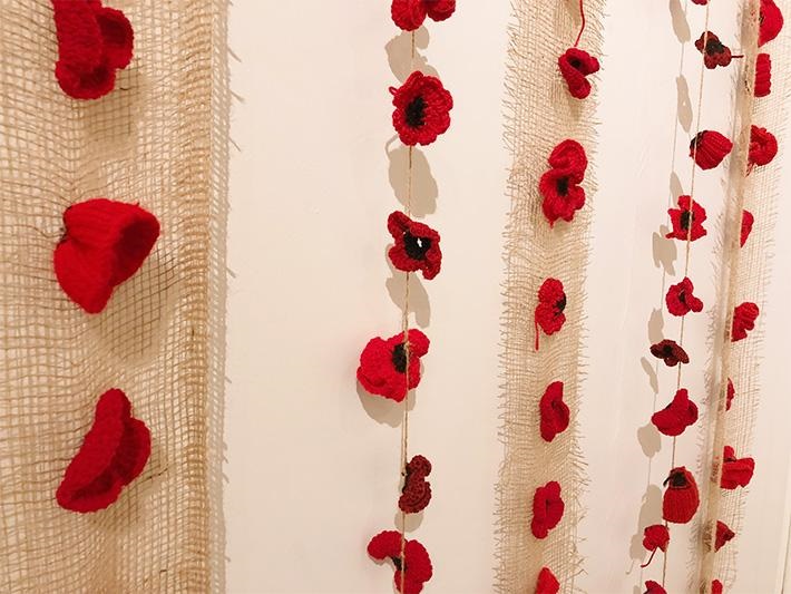 Fake poppies on strings and nets hung on a white wall 