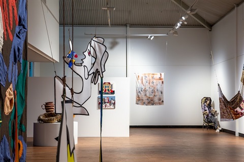 Installation view of textile exhibition with colourful artworks suspended and hung on the walls