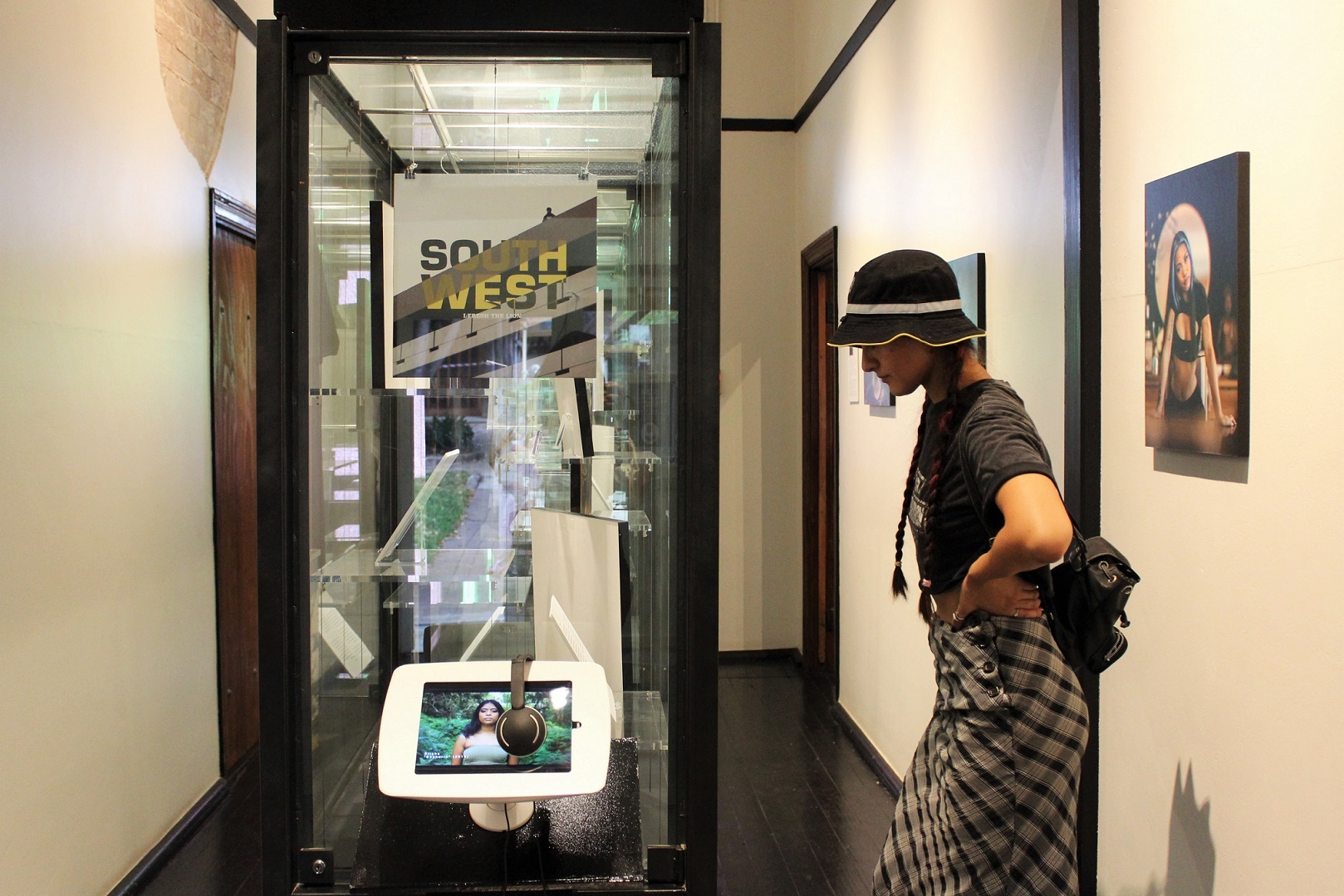 Visitor with hat looking at museum display case. Record cover displayed with the title SOUTH WEST and tablet playing music videos.