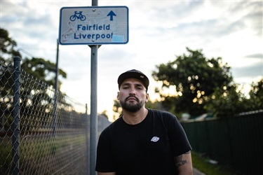 Portrait of a man wearing a cap posing outdoors underneath a streetsign for indicating Fairfield and Liverpool
