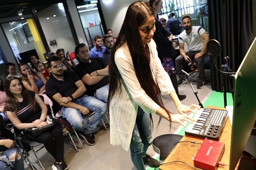 Crowd of guests seated in rows, watching young woman smiling and playing on a miniature keyboard 