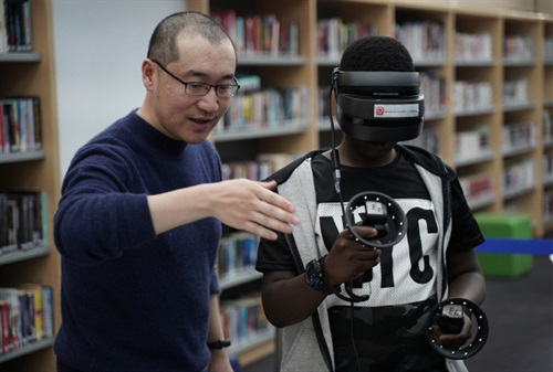 Man instructing virtual reality activity to a young person wearing head set and hand controllers 